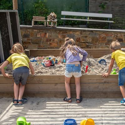 Trois enfants penchés sur le grand bac à sable de la cour