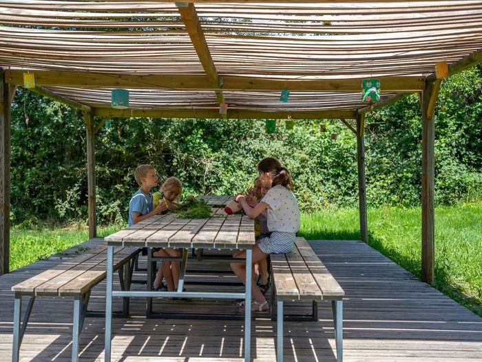 Des enfants travaillent autour d'une table sous la pergola, au milieu de la verdure